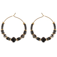 Boucles d'oreilles créoles en acier doré surmontées de perles cylindriques heishi en acier doré et caoutchouc de couleur noire, de perles de couleur noire et d'une pierre en forme de croix de couleur noire. 