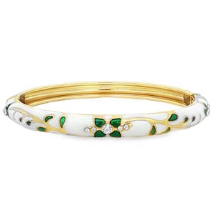 Ce bracelet se présente sous la forme d'un jonc articulé en métal doré, affichant un style à la fois sophistiqué et printanier. Sa structure est recouverte d'un émail blanc immaculé qui sert de toile de fond à des ornements délicats. Des volutes dorées serpentent le long du jonc, évoquant des tiges de fleurs. Elles sont ponctuées de petites feuilles en émail vert émeraude translucide, apportant une touche de couleur vive et organique. Le bijou est rehaussé de plusieurs cristaux scintillants de différentes tailles. Système de charnière discret permettant d'enfiler et de retirer le bijou avec facilité tout en assurant un maintien sécurisé au poignet.