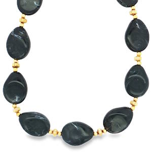 Ce collier de perles en acier doré est orné de perles noires ovales taillées en cabochon. Leurs teintes profondes et leurs reflets subtils captivent le regard. Ce bijou artisanal évoque l'élégance intemporelle et le raffinement discret. Un accessoire parfait pour sublimer votre style avec une touche de mystère et de sophistication. Fermoir mousqueton avec 5 cm de rallonge.