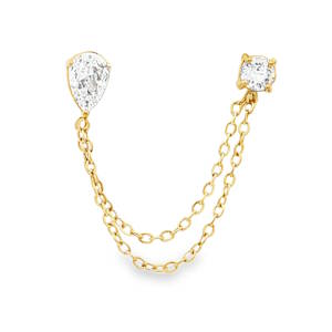Cette pièce sophistiquée revisite le concept du piercing multiple avec une touche de haute joaillerie. Conçue pour relier deux perforations du lobe ou du cartilage (hélix), elle allie éclat classique et design contemporain. L'ensemble se compose de deux puces distinctes reliées par un jeu de chaînes pendantes et chacune sertie d'un cristal de taille poire (en forme de goutte), apportant une touche de finesse et d'allongement. Et d'un cristal de taille brillante (rond), offrant un éclat maximal et une structure équilibrée.