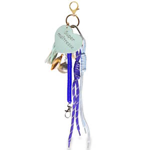 Ce porte-clés est un accessoire coloré et multifonctionnel, conçu comme un cadeau attentionné. Le style est résolument estival et artisanal, mélangeant des textures variées (corde, métal, plastique, cuir) dans une palette de couleurs tournant autour du bleu, du violet et du vert menthe. Une pièce en simili cuir de couleur vert menthe en forme de cœur. Il porte l'inscription manuscrite Super maîtresse, ce qui en fait un cadeau idéal pour la fin d'année scolaire.