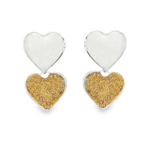 Ces ravissantes boucles d'oreilles pendantes célèbrent le romantisme avec une touche de modernité. Conçues en argent 925/000, elles se distinguent par un jeu de textures et de contrastes raffiné. Chaque boucle est formée de deux cœurs superposés, reliés par une articulation discrète qui permet un léger mouvement fluide. Apporte une touche de lumière chaleureuse grâce à un insert scintillant couleur dorée. Sa texture granuleuse, rappelant de la poussière d'étoiles ou du fini pailleté, crée un contraste saisissant avec la sobriété du premier cœur. L'équilibre parfait entre la brillance de l'argent et le scintillement du doré fait de ce modèle un cadeau idéal pour exprimer un sentiment sincère.